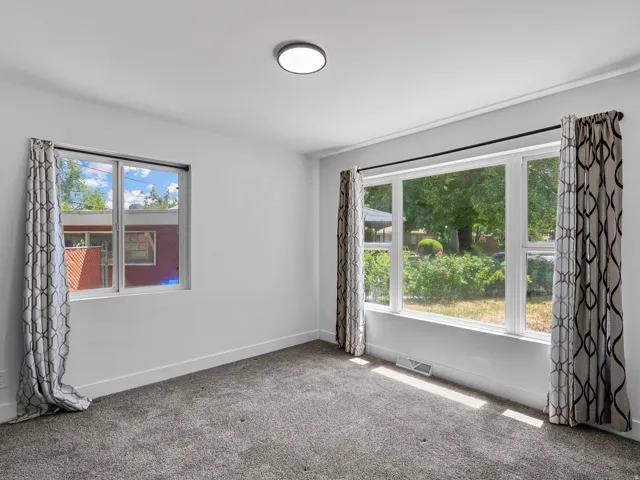 Bright interior space featuring a large picture window, a secondary window, neutral gray carpeting, white baseboards, and a flush-mount ceiling light