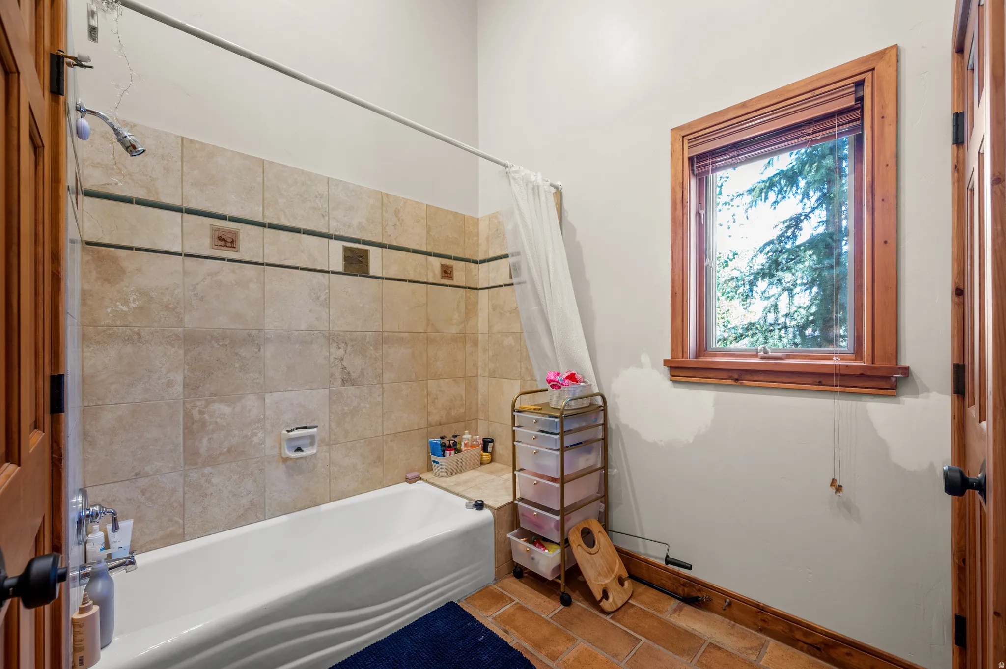 Bathroom featuring an alcove bathtub with tiled surround, a window with wood trim, and terracotta-style flooring