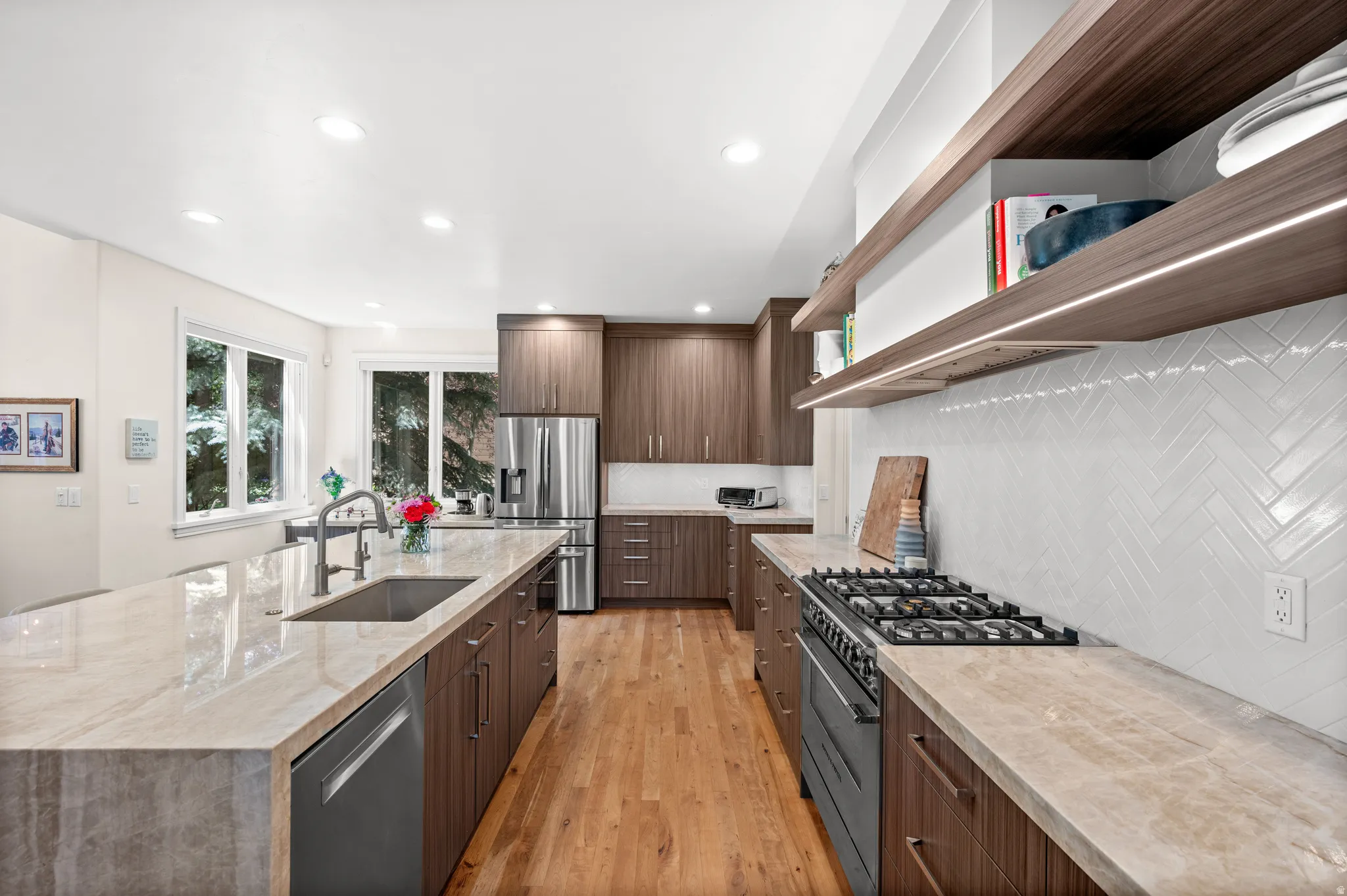 Gourmet kitchen featuring a large island with an undermount sink, stone countertops, wood-finish cabinetry, stainless steel appliances, and wood-finish flooring