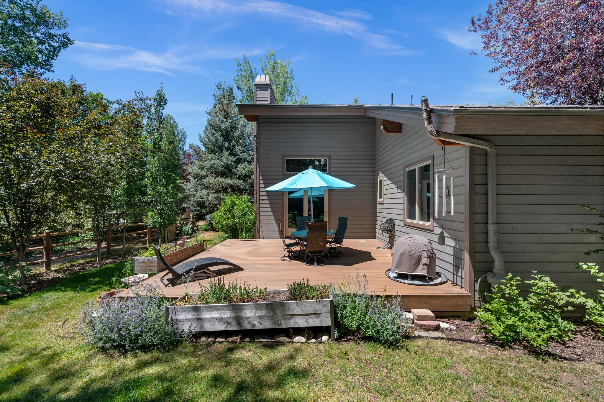 Spacious outdoor deck featuring wood-finish flooring, surrounded by lush greenery and mature trees