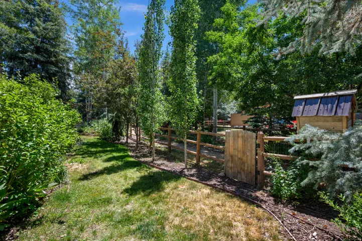 Fenced backyard featuring a wooden gate, split-rail fencing, mature trees, and established landscaping
