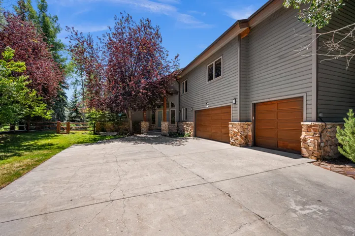 Spacious concrete driveway featuring a two-car garage with wood-paneled doors and stone accents