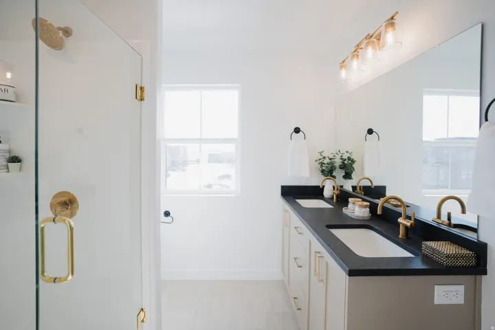 Bathroom featuring a dual vanity with undermount sinks, black countertops, and brushed gold fixtures
