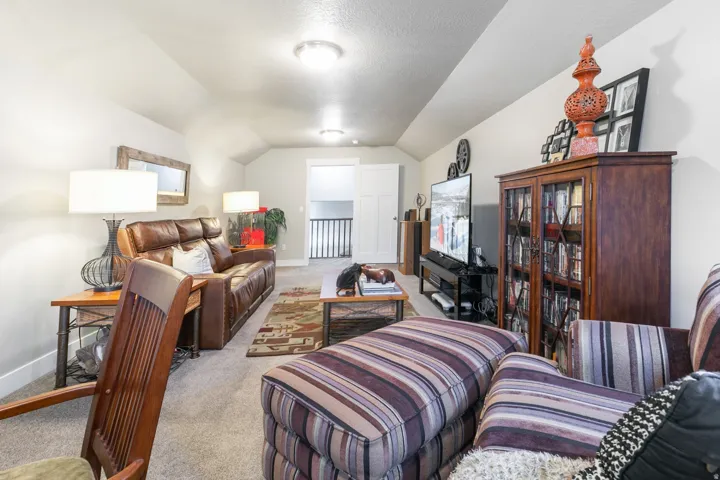 Carpeted bonus room featuring sloped ceilings, recessed lighting, a wooden built-in cabinet with glass doors, and a partial view of a white balustrade