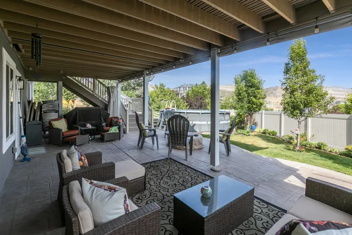 Covered patio with stamped concrete flooring, exposed wood ceiling joists, and a two-story wood staircase