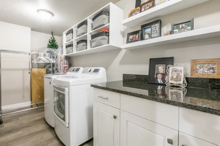 Laundry area featuring wood-finish flooring, white cabinetry, dark stone countertops, and open shelving