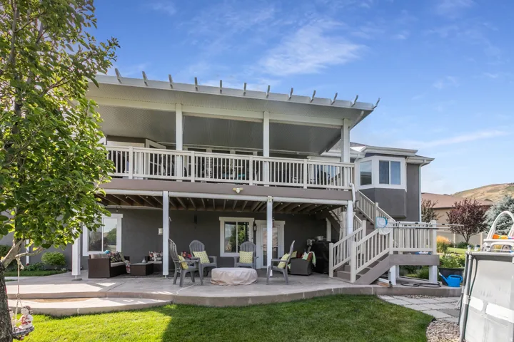Multi-level exterior featuring a ground-level patio, a second-story balcony with a pergola, and stucco siding