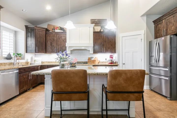 Spacious kitchen featuring a large island with a stone countertop, stainless steel appliances, a white tile backsplash, and a vaulted ceiling