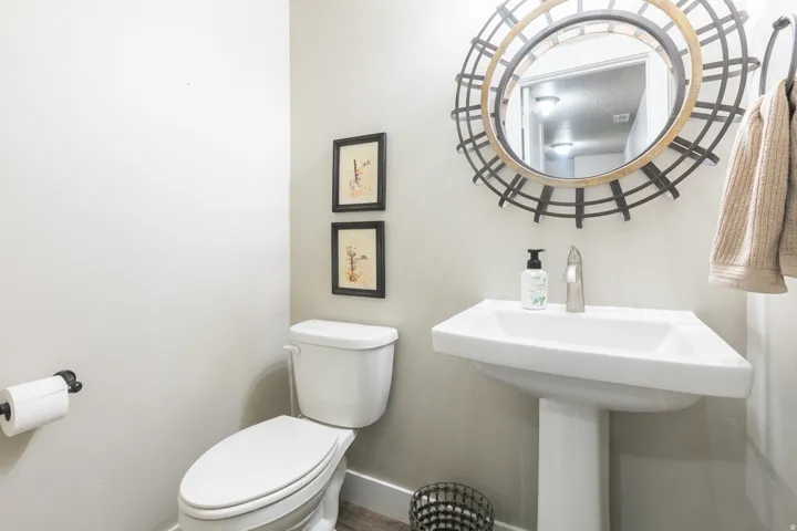 Pedestal sink with a polished chrome faucet, round decorative mirror, toilet, and wood-finish flooring