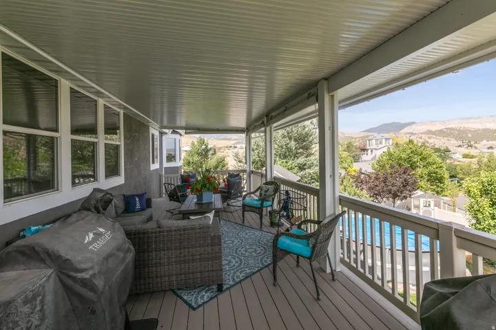 Spacious covered deck featuring composite wood-finish flooring, white railing, and a textured wall