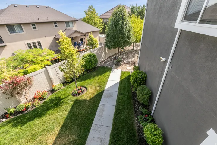 Side yard featuring a concrete pathway, manicured lawn, and planted garden beds