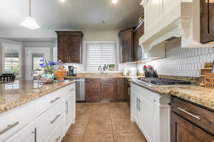 Kitchen featuring an expansive island with granite countertops, stainless steel appliances, a gas range with a decorative range hood, two-tone cabinetry, and a geometric tile backsplash