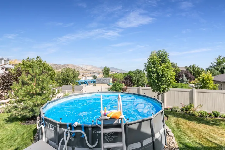 Expansive backyard featuring an above-ground pool, level lawn, established landscaping, and a privacy fence