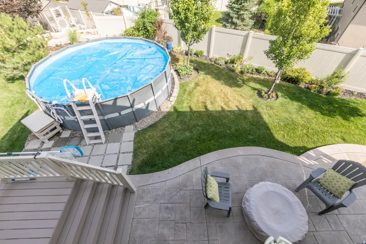 Backyard featuring a round above-ground pool with stone-look surround, a stamped concrete patio, and a tiered deck with wood-finish decking