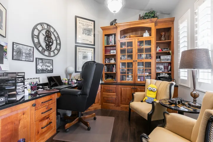 Dedicated office space featuring built-in wood cabinetry with glass-front uppers, a built-in desk with a black countertop, and dark wood-finish flooring
