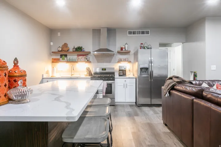 Kitchen featuring a long island with a white patterned countertop, stainless steel appliances, light wood-finish flooring, white cabinetry, and open shelving