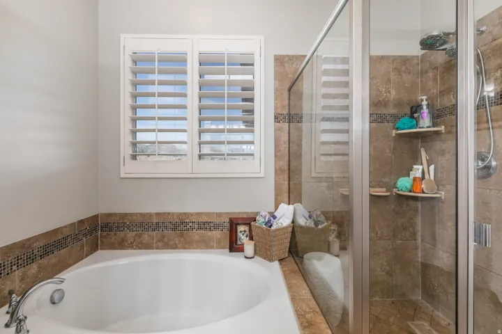 Soaking tub with chrome fixtures, surrounded by neutral-toned tile with a decorative mosaic accent
