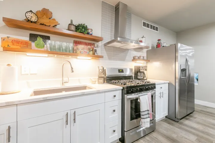 Kitchen featuring white shaker cabinetry, light-toned countertops, stainless steel appliances, and wood-finish open shelving