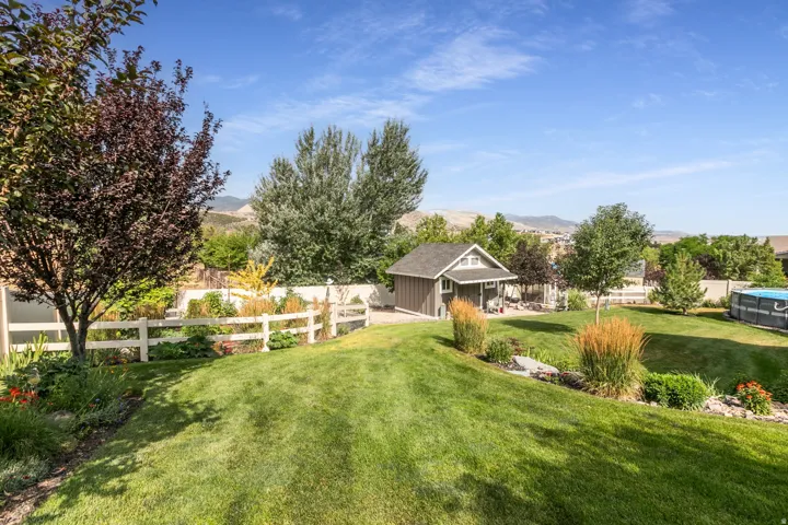 Expansive backyard featuring a lush lawn, mature trees, and a white fence
