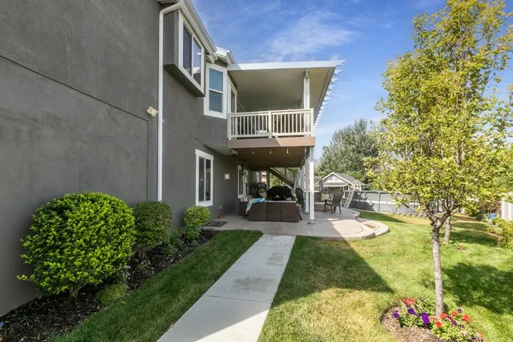 Rear exterior featuring a grey stucco finish, a covered patio, and an upper-level balcony with white railings