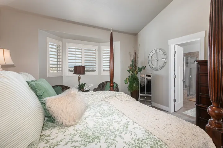Bedroom featuring a bay window with plantation shutters, vaulted ceilings, and an en-suite bathroom entrance with a glass-enclosed shower