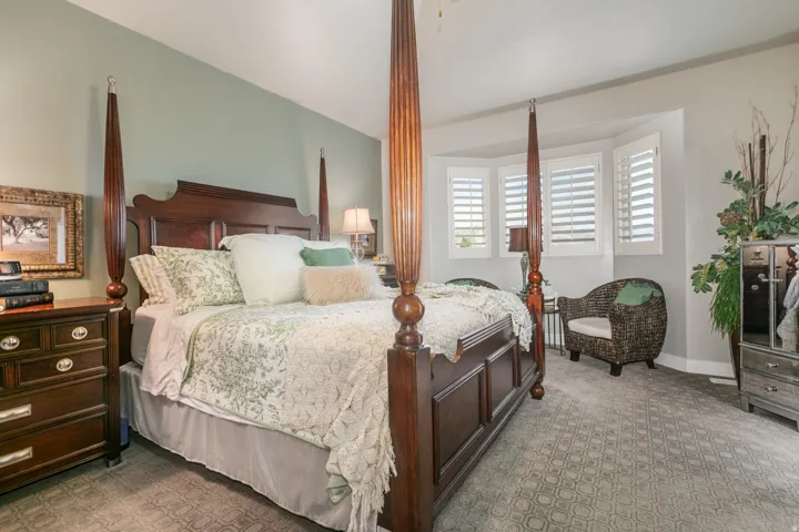 Spacious room with patterned carpeting and a bay window featuring white plantation shutters
