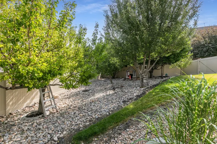 Sloping backyard featuring mature trees, rock ground cover, and a manicured grassy strip