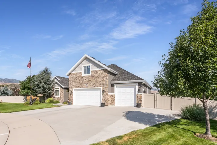 Exterior featuring stone facade, two white garage doors, a light beige privacy fence, and a concrete driveway
