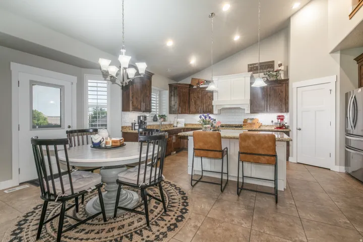Spacious kitchen featuring a two-toned cabinetry scheme, granite countertops, tile flooring, and a vaulted ceiling