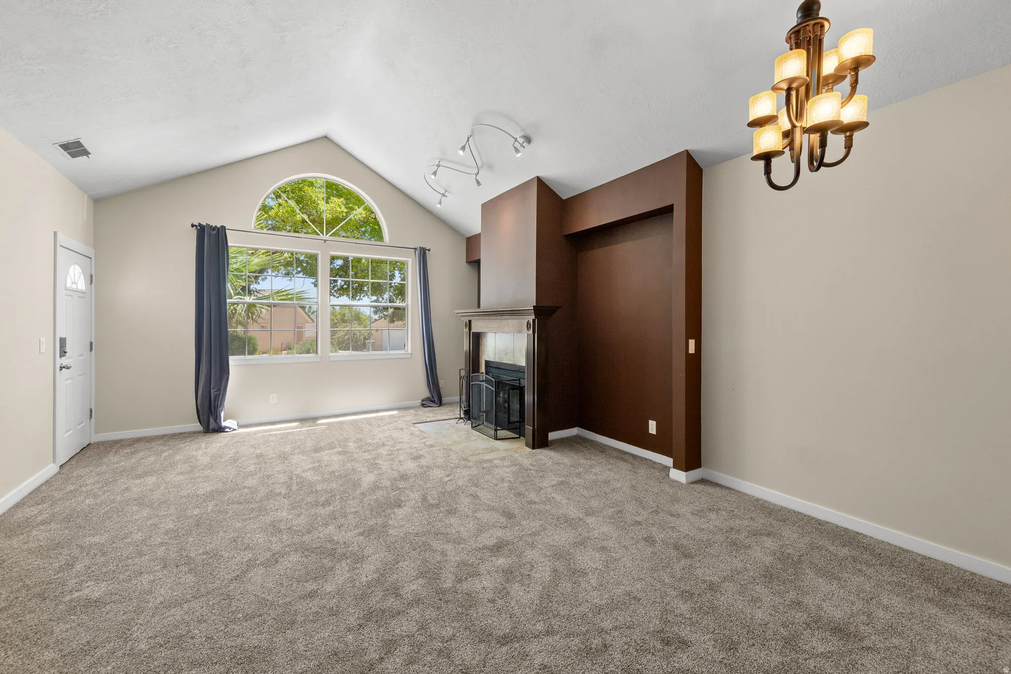 Vaulted ceiling living area featuring a fireplace with a mantel, arched transom window, track lighting, and a multi-arm chandelier