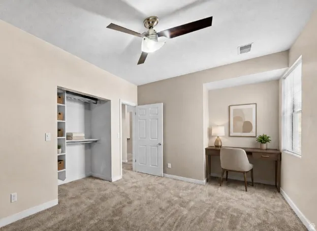 Carpeted room featuring a ceiling fan with light, a built-in closet with shelving, a window with blinds, and a paneled interior door