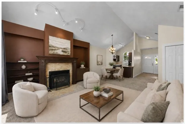 Living area with a vaulted ceiling, track lighting, and a fireplace featuring a wood mantel and stone surround
