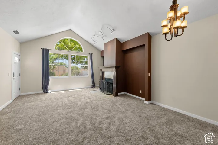 Vaulted ceiling living area featuring a fireplace with a mantel, arched transom window, track lighting, and a multi-arm chandelier