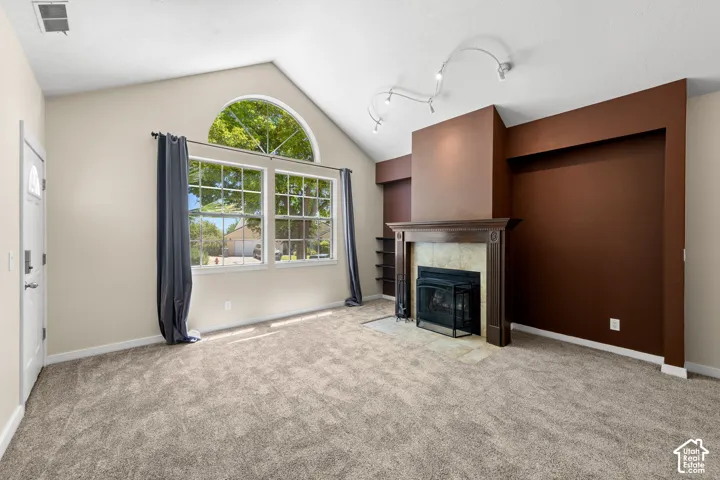 Living area featuring vaulted ceilings, a prominent fireplace with wood-finish mantel and tile surround, large windows with an arched transom, track lighting, and soft gray carpeting