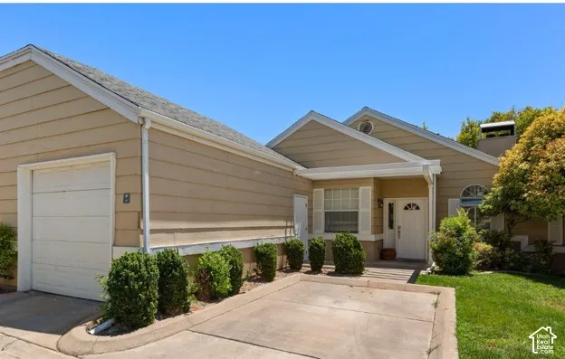 Exterior featuring tan siding, a two-car garage, a covered front entry, and a mature tree