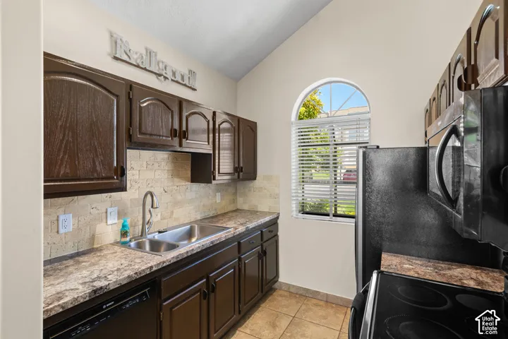 Kitchen featuring dark wood cabinetry, a double basin stainless steel sink, and a light-toned stone tile backsplash