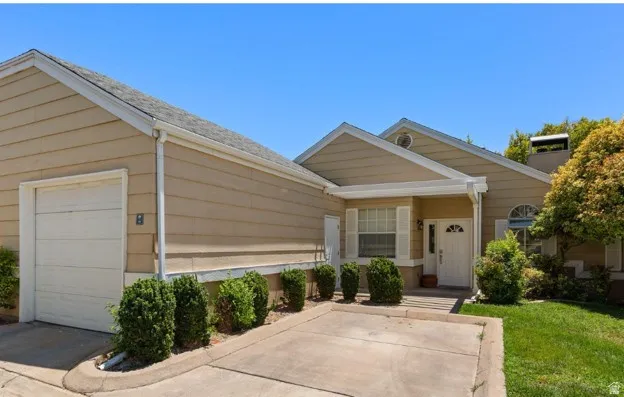 Exterior featuring tan siding, a two-car garage, a covered front entry, and a mature tree