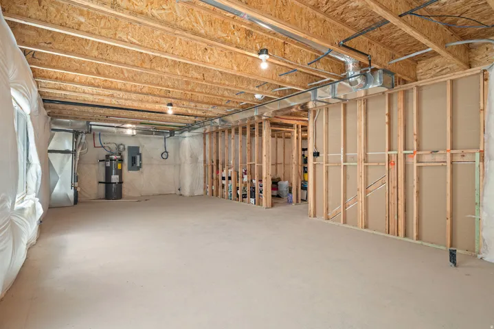 Expansive unfinished basement featuring concrete flooring, exposed wood joists, framed walls, a water heater, and a visible electrical panel