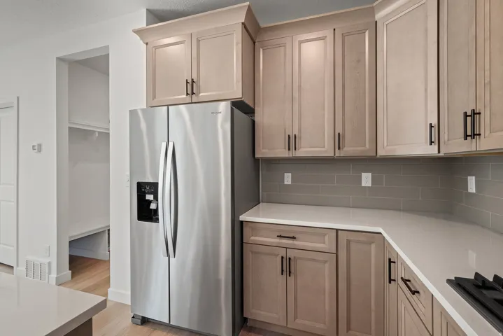 Modern kitchen featuring light-toned cabinetry with black hardware, white countertops, and a gray subway tile backsplash