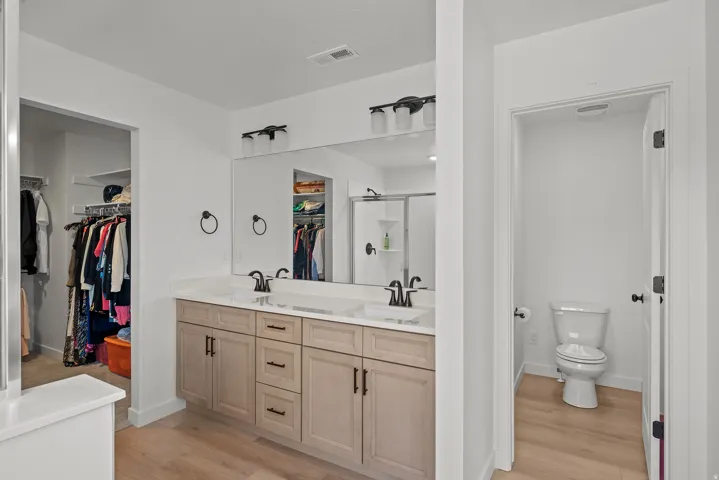 Double vanity with light wood-finish cabinetry, white countertops, and black hardware