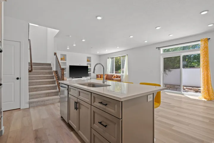 Kitchen island with integrated sink and dishwasher, light wood-finish flooring, recessed lighting, built-in shelving, and sliding glass door access to an exterior area