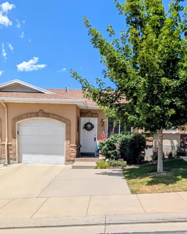 Property exterior featuring a stucco facade with stone accents, an arched garage entrance, a white entry door, and a mature tree