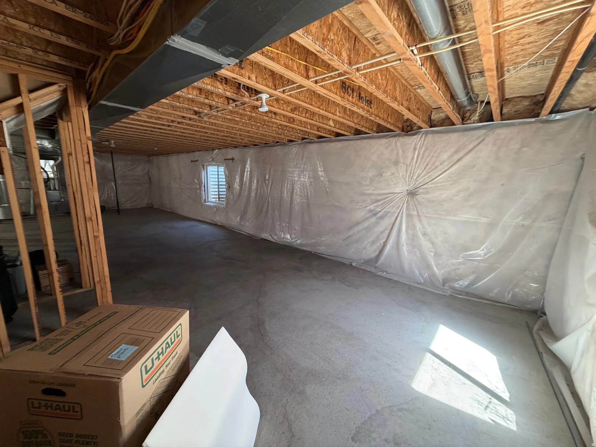 Unfinished basement with exposed ceiling joists, concrete flooring, and a framed window opening
