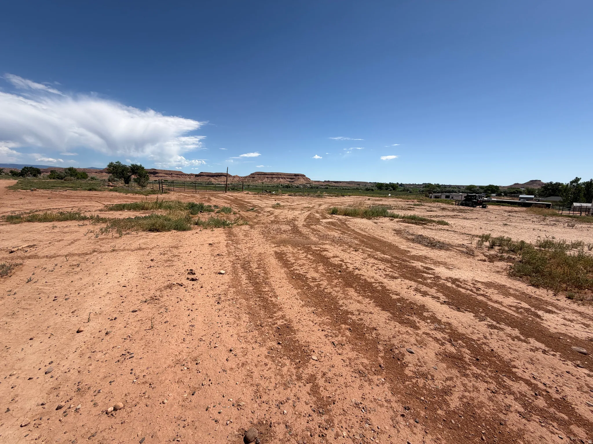 Expansive land featuring a dirt road, sparse vegetation, and distant red rock formations