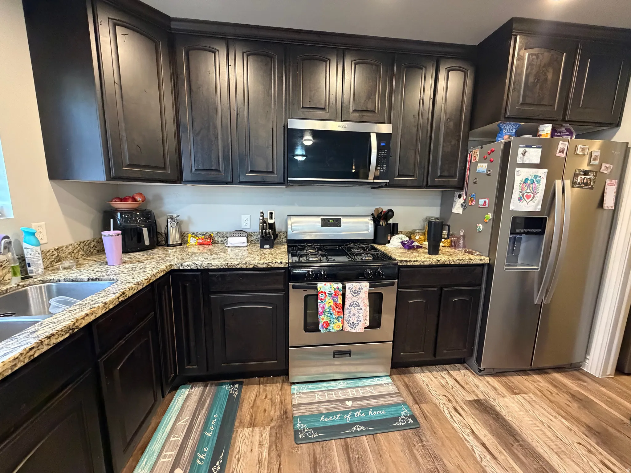 Kitchen featuring dark wood cabinetry, granite-style countertops, stainless steel appliances, a double basin sink, and wood-finish flooring