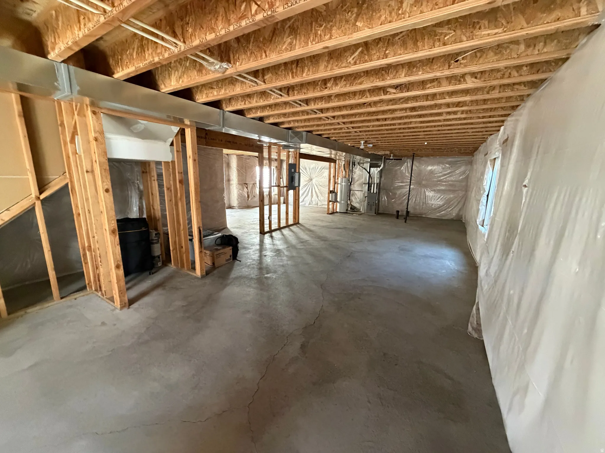 Unfinished basement space featuring exposed wood joists, concrete flooring, interior framing, and foil-faced insulation