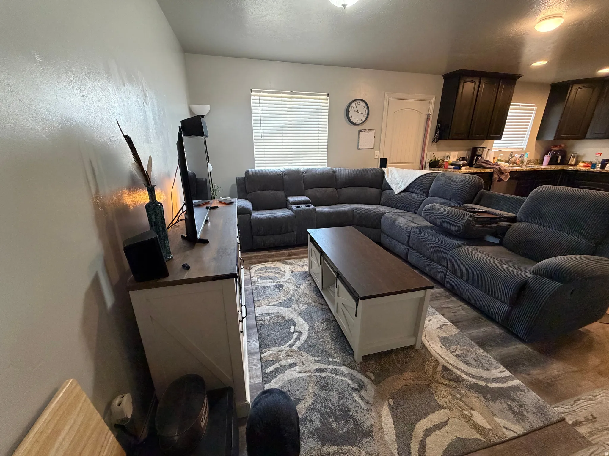 Open-concept living area featuring wood-finish flooring, a contemporary area rug, and a built-in media console with a wood-finish top
