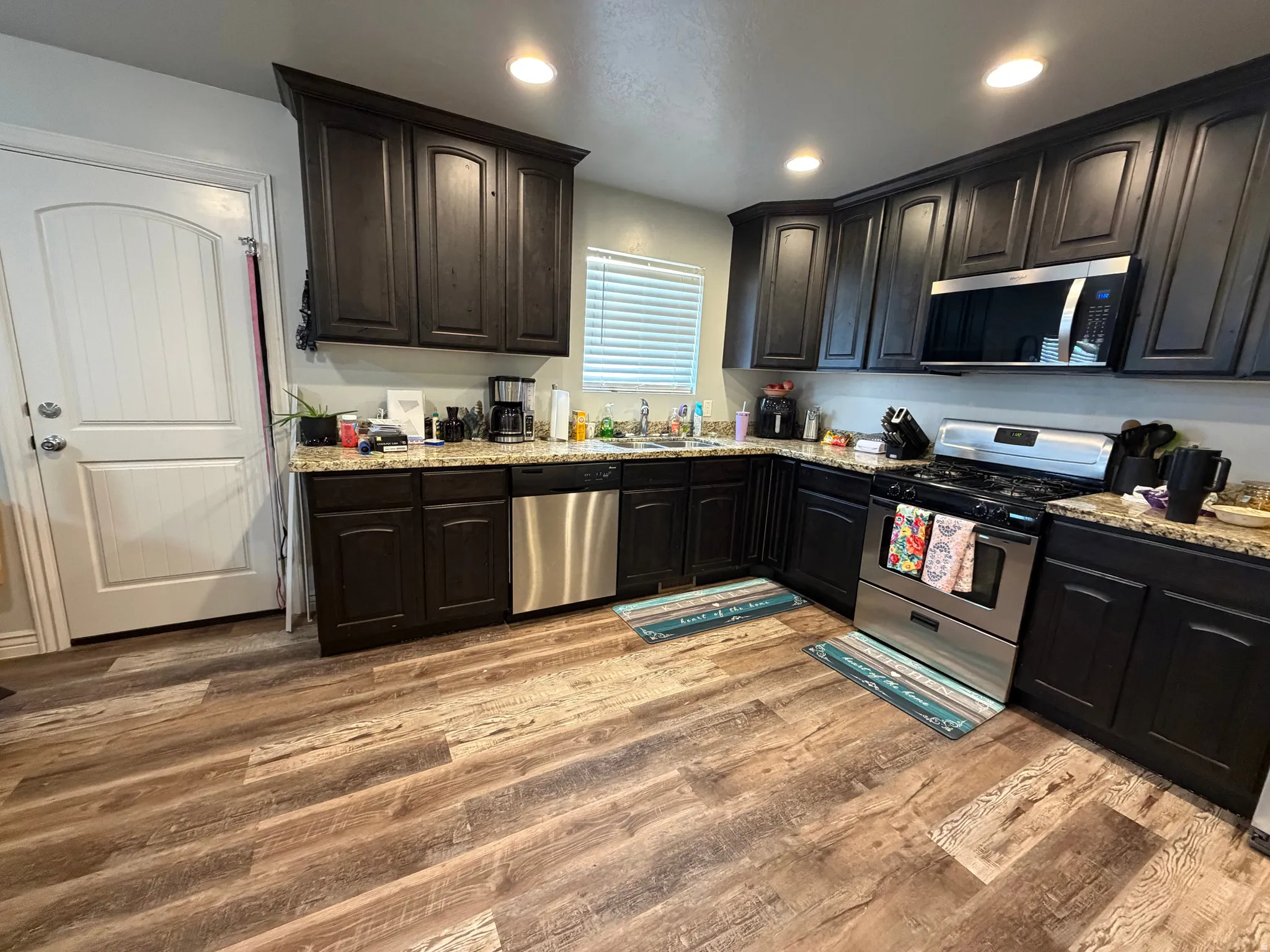 Kitchen featuring dark wood cabinetry, light-toned countertops, wood-finish flooring, recessed lighting, and stainless steel appliances
