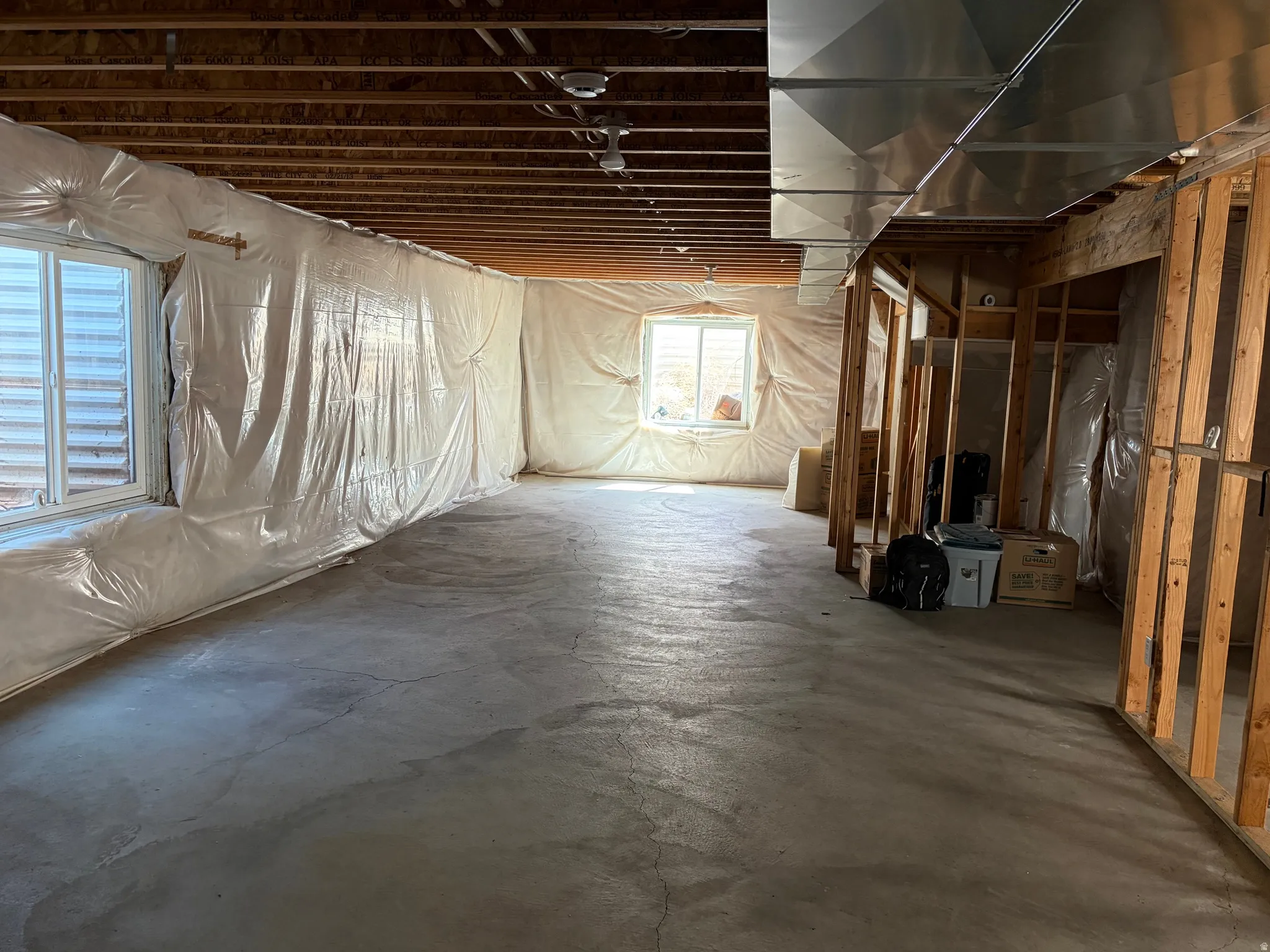 Unfinished basement featuring exposed wood joists, concrete flooring, two windows, wall insulation, and visible HVAC ductwork