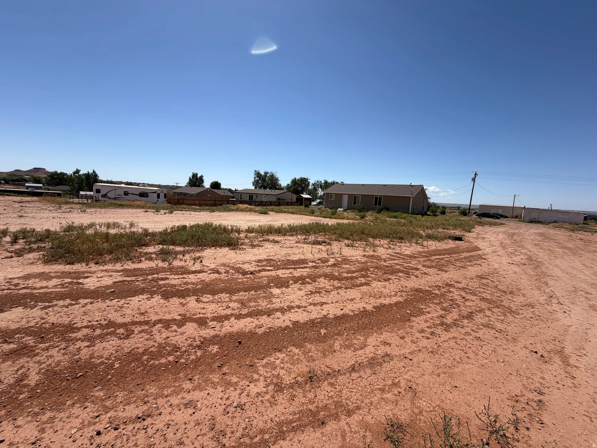 Expansive open lot featuring a clear sky overhead and a distant residential structure